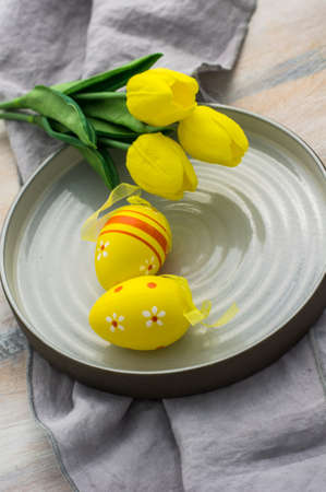 Table setting for Easter dinner with tulips and eggs on white wooden table