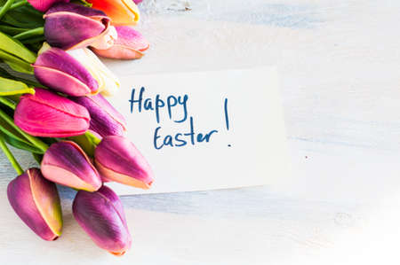Easter festive frame with eggs, tulips and easter bunny on white rustic wooden table with copyspaceの写真素材