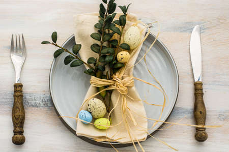 Table setting for Easter dinner with tulips and eggs on white wooden table