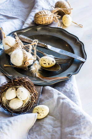 Table setting for Easter dinner with eggs on white wooden table