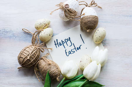 Easter festive frame with eggs, tulips and easter bunny on white rustic wooden table with copyspace