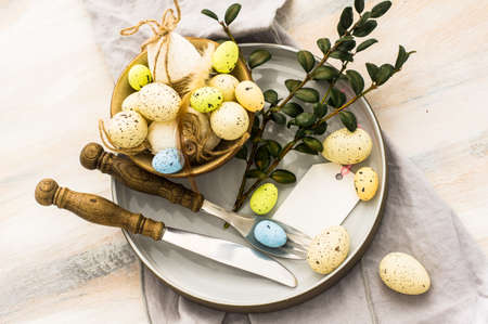 Table setting for Easter dinner with tulips and eggs on white wooden table