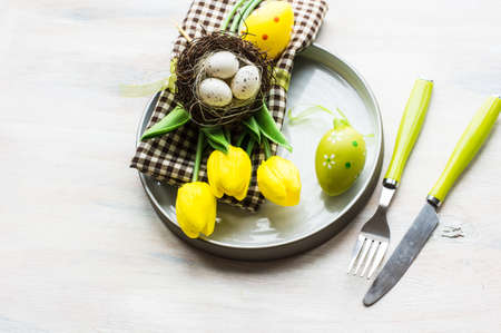 Table setting for Easter dinner with tulips and eggs on rustic wooden table