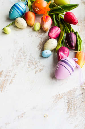Easter festive frame with eggs, tulips and easter bunny on white rustic wooden table with copyspace