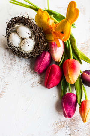 Easter festive frame with eggs, tulips and easter bunny on white rustic wooden table with copyspace