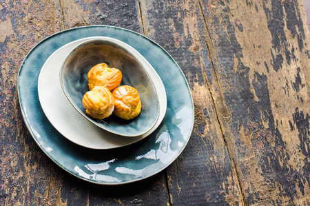 French dessert profiterole or eclair on a rustic plate with vintage silverware on dark rustic table...