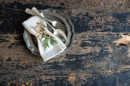 Table setting with fresh rosemary and rustic silverware on dark wooden tableの写真素材