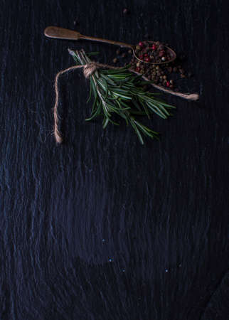 Organic spices on dark stone background - rosemary and different colors peppercornの写真素材