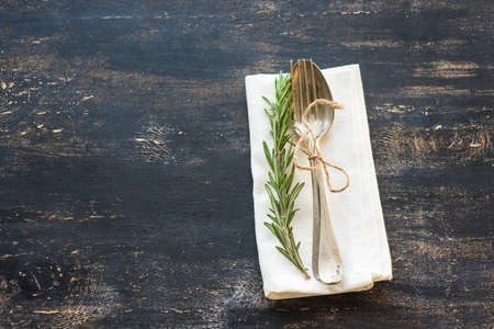 Table setting with fresh rosemary and rustic silverware on dark wooden tableの写真素材