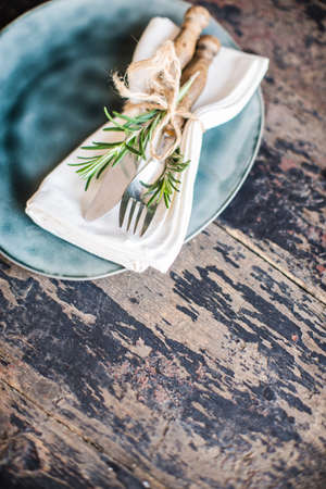 Table setting with fresh rosemary and rustic silverware on dark wooden tableの写真素材