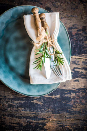 Table setting with fresh rosemary and rustic silverware on dark wooden tableの写真素材