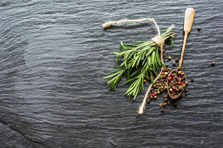 Organic spices on dark stone background - rosemary and different colors peppercornの写真素材