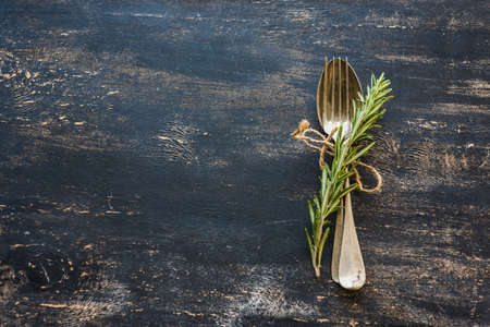 Table setting with fresh rosemary and rustic silverware on dark wooden tableの写真素材