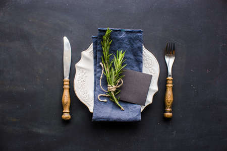 Table setting with fresh rosemary and rustic silverware on dark wooden tableの写真素材