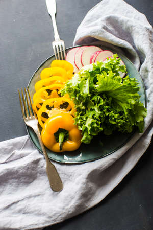 Healthy food concept yellow  sliced bell pepper, radish vegetables and letuce leaves on a rustic plateの写真素材