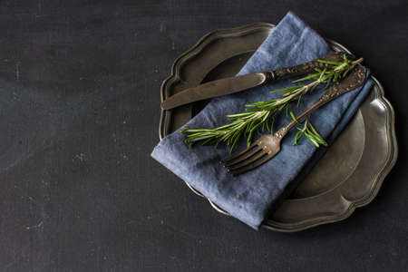 Rustic table setting with empty plate and vintage silverware decorated with fresh rosemary on dark wooden tableの写真素材
