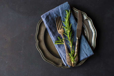 Rustic table setting with empty plate and vintage silverware decorated with fresh rosemary on dark wooden tableの写真素材