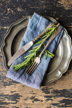 Rustic table setting with empty plate and vintage silverware decorated with fresh rosemary on dark wooden tableの写真素材