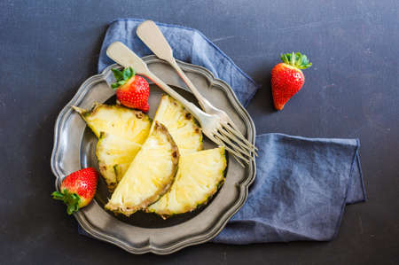 Vintage metal plate full of strawberry and slices of pineapple on dark wooden table