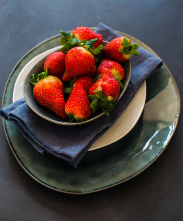 Ceramic bowl full of strawberries on dark wooden tableの写真素材