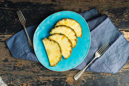 Rustic plate full of pineapple slices on dark wooden table with copyspaceの写真素材