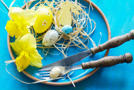 Festive table setting for Easter dinner with bright easter eggs and yellow daffodilsの写真素材