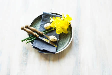 Festive table setting for Easter dinner with bright easter eggs and yellow daffodilsの写真素材
