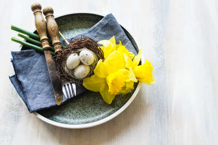 Festive table setting for Easter dinner with bright easter eggs and yellow daffodilsの写真素材