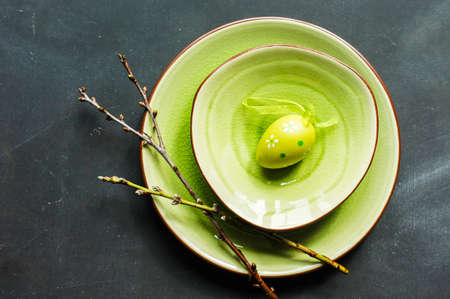 Festive table setting for Easter dinner with bright easter eggs on green platesの写真素材