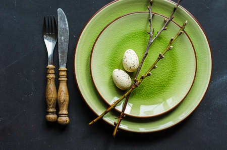 Festive table setting for Easter dinner with bright easter eggs on green platesの写真素材