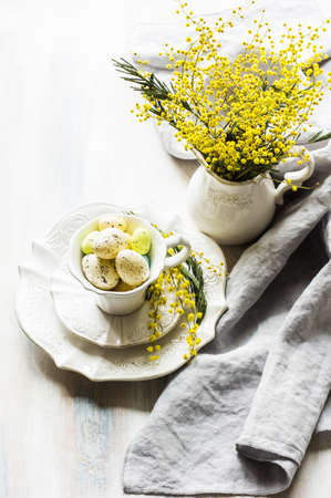 Festive table setting for Easter dinner with bright easter eggs and mimosa flowers on rustic plate