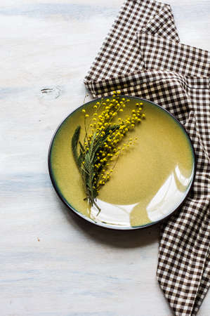Festive table setting for Easter dinner with bright easter eggs and mimosa flowers on rustic plateの写真素材