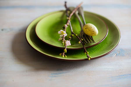 Table setting for Easter dinner with blooming cherry tree branch and eggs on bright green platesの写真素材