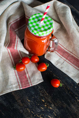 Organic tomatoes juice in a bottle with straw and fresh cherry tomatoes and parsley herb on dark wooden tableの写真素材