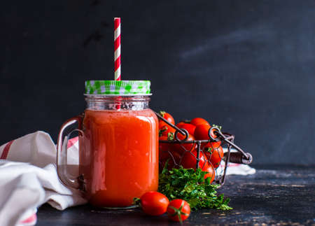 Organic tomatoes juice in a bottle with straw and fresh cherry tomatoes and parsley herb on dark wooden tableの写真素材