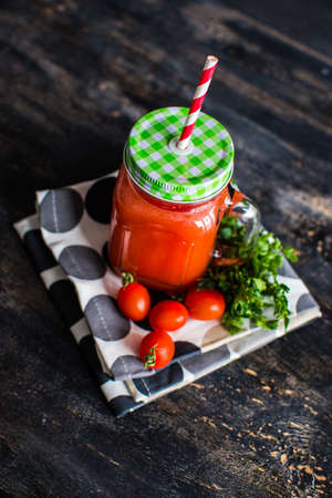 Organic tomatoes juice in a bottle with straw and fresh cherry tomatoes and parsley herb on dark wooden tableの写真素材