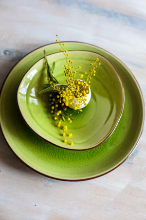 Table setting for Easter dinner with blooming mimosa acacia flowers and eggs on bright green plates