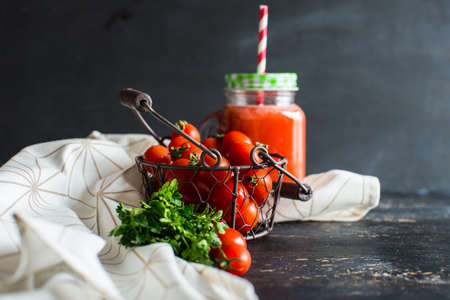 Organic tomatoes juice in a bottle with straw and fresh cherry tomatoes and parsley herb on dark wooden tableの写真素材