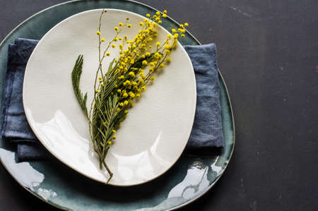 Festive table setting for Easter dinner with bright easter eggs and mimosa flowers on rustic plateの写真素材