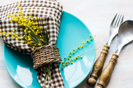 Festive table setting for Easter dinner with bright easter eggs and mimosa flowers on rustic plateの写真素材