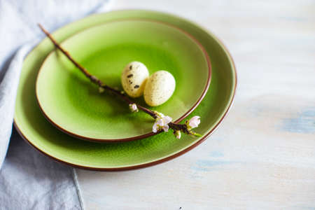 Table setting for Easter dinner with blooming cherry tree branch and eggs on bright green platesの写真素材