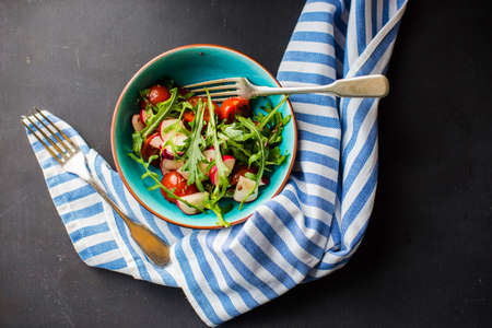 Spring healthy salald with fresh organic tomatoes, radish and rukkola herb on rustic plate with napkin and silverwareの写真素材