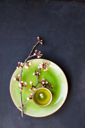 Cup of green tea and peach blossom on dark rustic table as a spring time conceptの写真素材