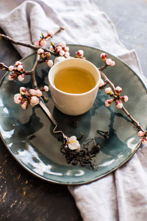Cup of green tea and peach blossom on dark rustic table as a spring time conceptの写真素材