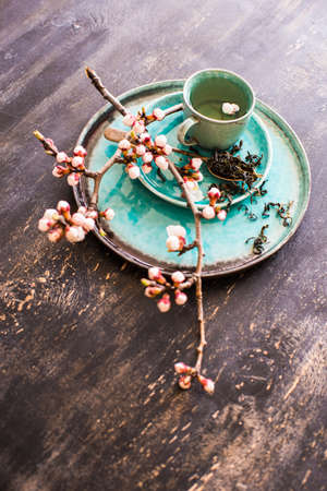 Cup of green tea and peach blossom on dark rustic table as a spring time conceptの写真素材