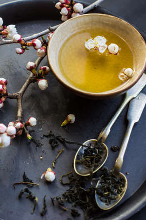 Cup of green tea and peach blossom on dark rustic table as a spring time conceptの写真素材
