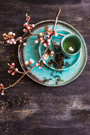 Cup of green tea and peach blossom on dark rustic table as a spring time conceptの写真素材