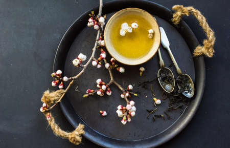 Cup of green tea and peach blossom on dark rustic table as a spring time conceptの写真素材