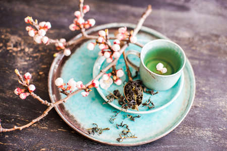 Cup of green tea and peach blossom on dark rustic table as a spring time conceptの写真素材