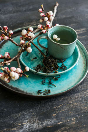 Cup of green tea and peach blossom on dark rustic table as a spring time conceptの写真素材
